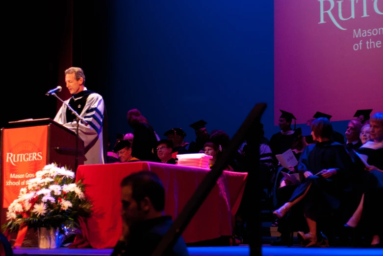 a man speaking in front of a bunch of graduates