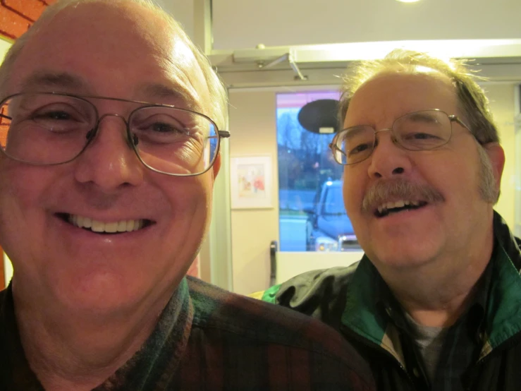 an older gentleman wearing glasses smiling while another guy looks on