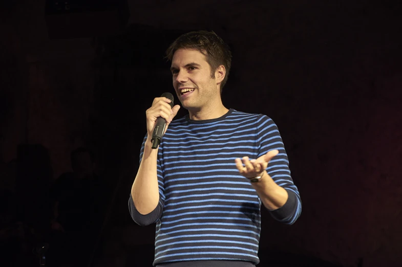 a man wearing a blue striped shirt talking into a microphone
