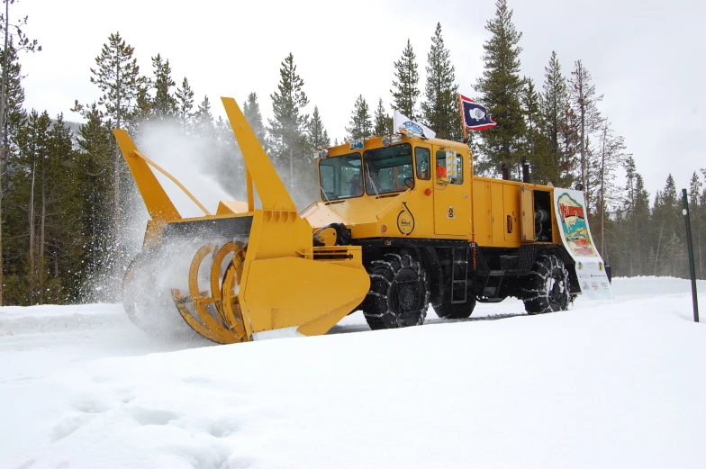 yellow snow plow with a large wheel working on a snowy hill