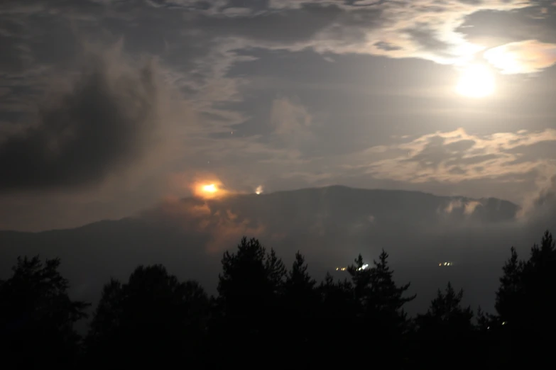 the sun in a grey sky with a tree line below