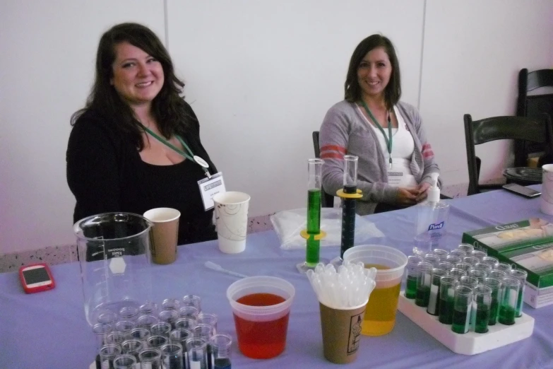 two women posing in front of a table full of plastic cups