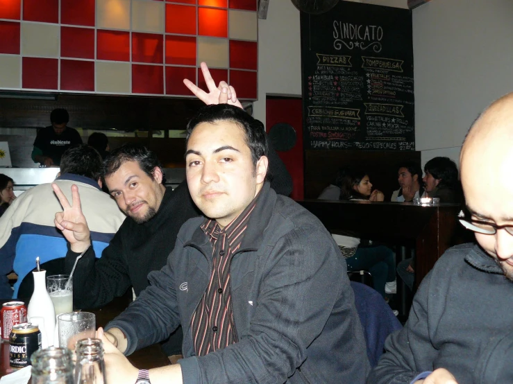 three men at a table drinking, one wearing a drink crown