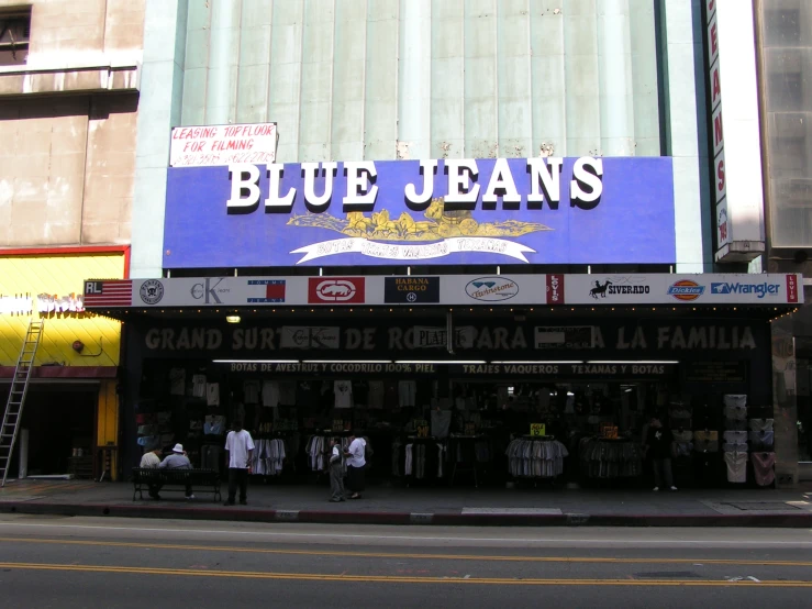 the blue jeans sign hangs from a building in front of several people standing on a sidewalk