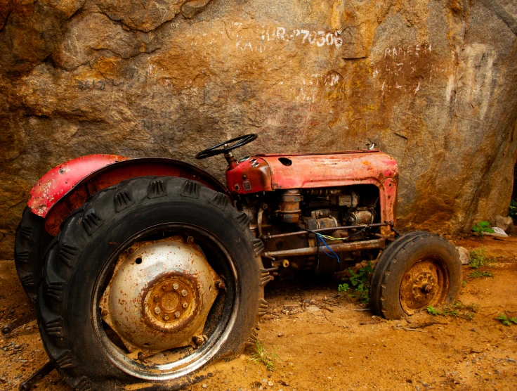 a red tractor sits in front of a rocky wall