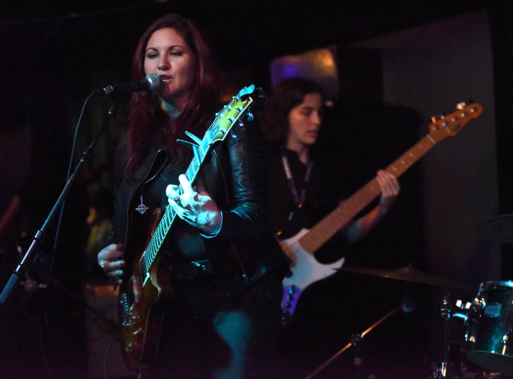 a girl in leather outfit singing and playing a guitar