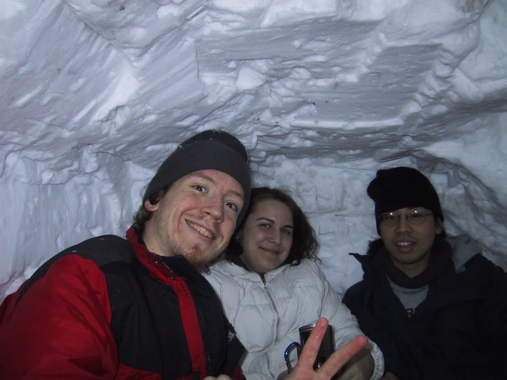 three people stand inside of a snow tunnel and gesture