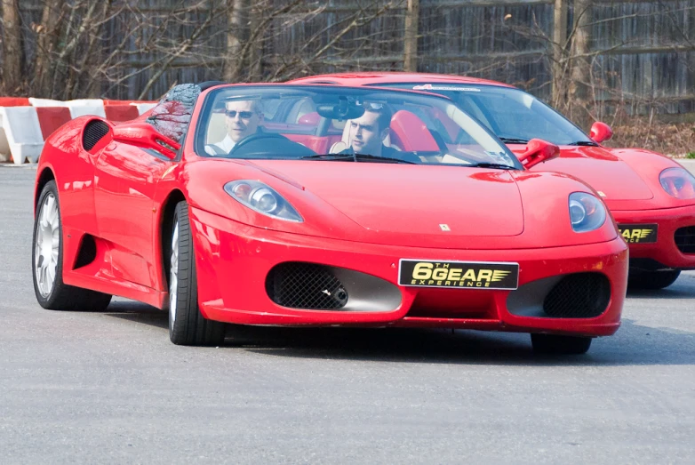 two men driving red sports cars down the road