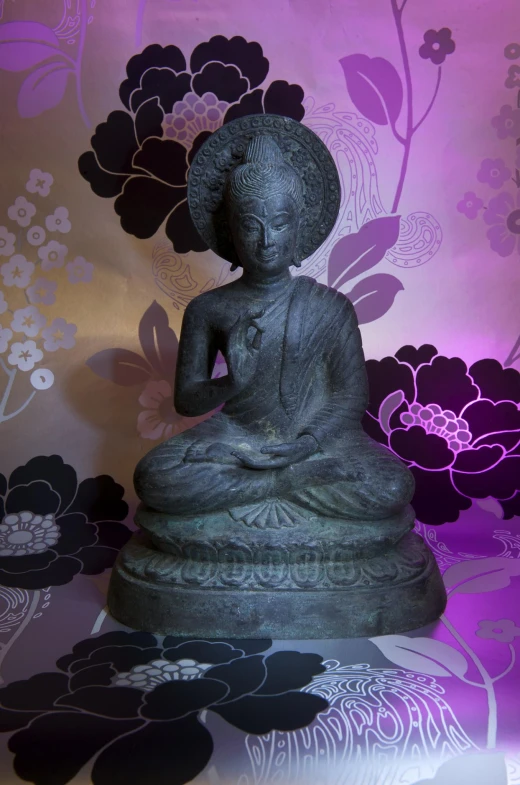 a buddha statue in front of a flowered wallpaper