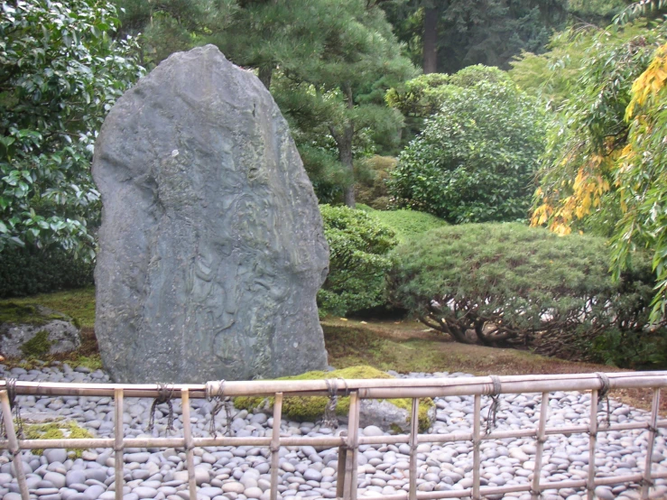 a rock sitting between two large rocks next to a bamboo fence