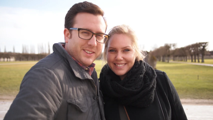 a man and woman pose together in front of a grassy area