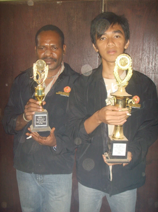 two men holding up trophies in their hands