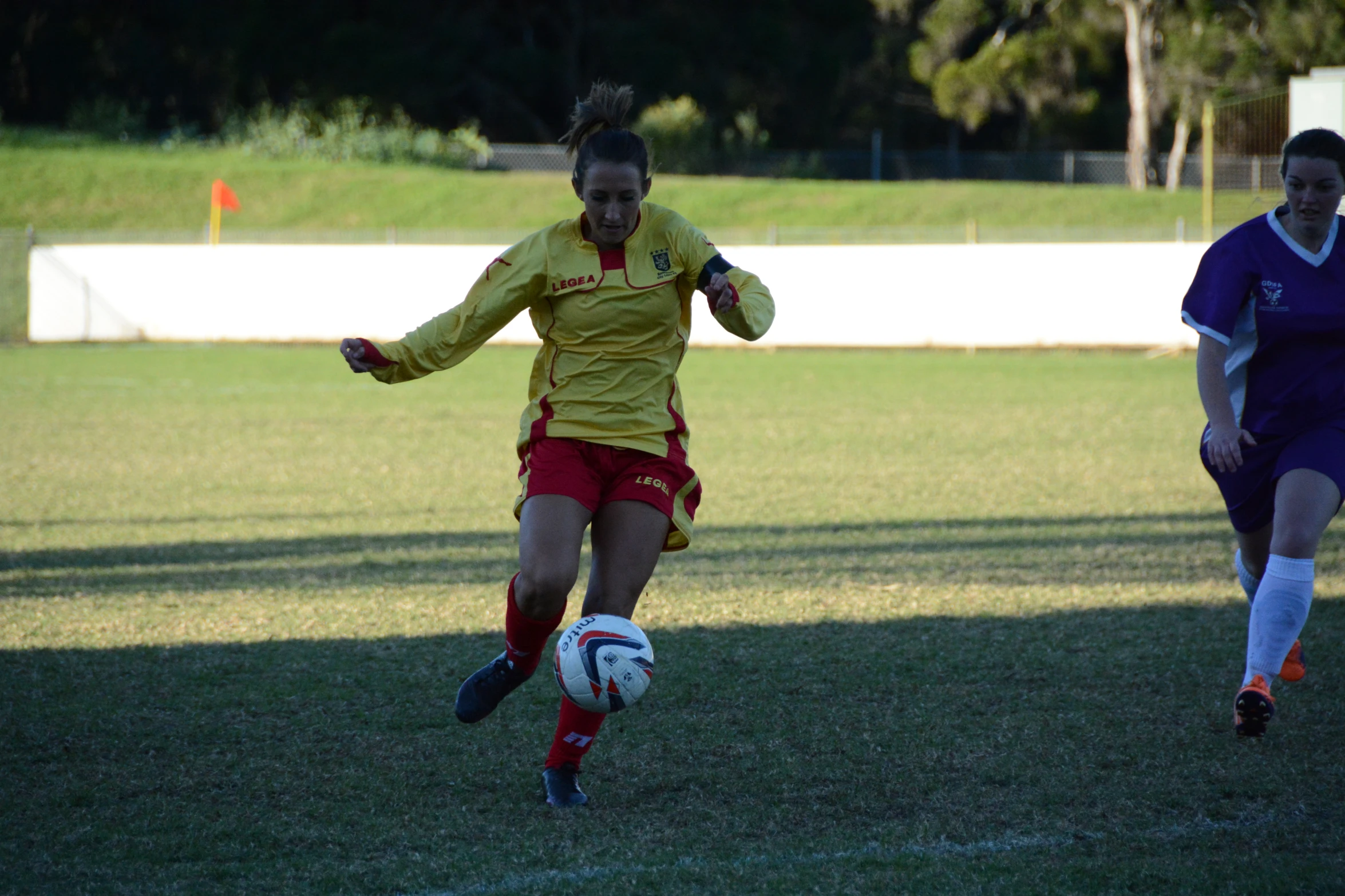 a girl on a field playing soccer with another woman running after her