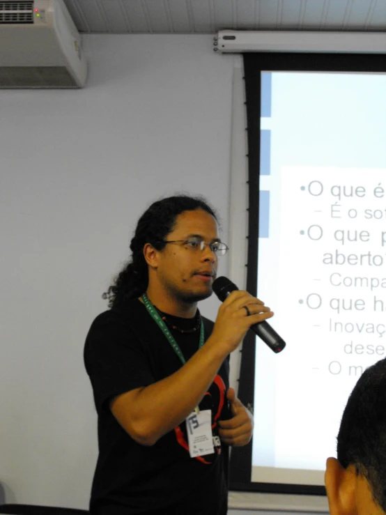 a man speaking into a microphone in front of a projection screen