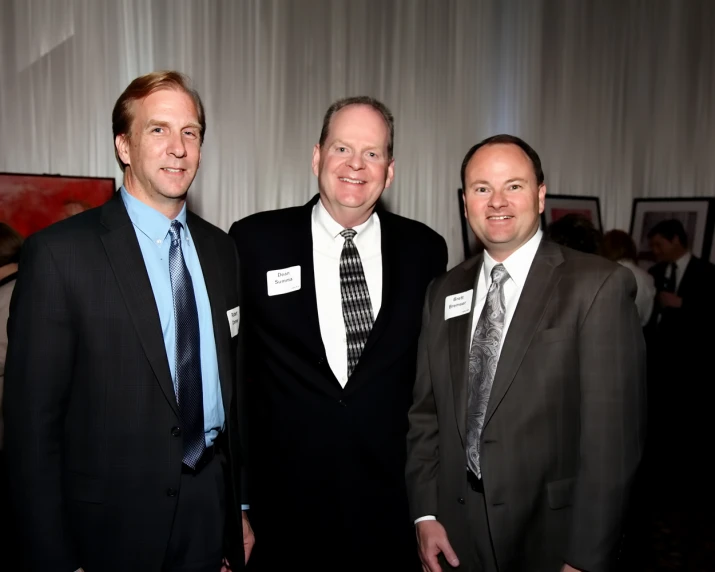 three men standing beside each other smiling for the camera