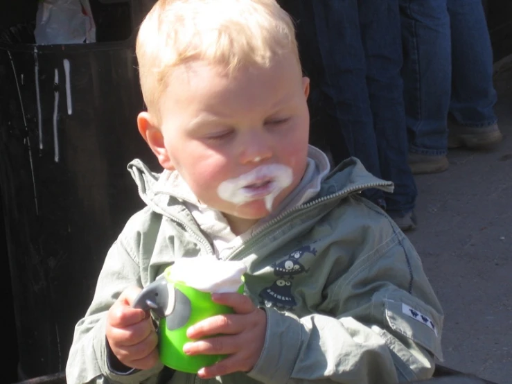 small child with ice cream on his face eating an object