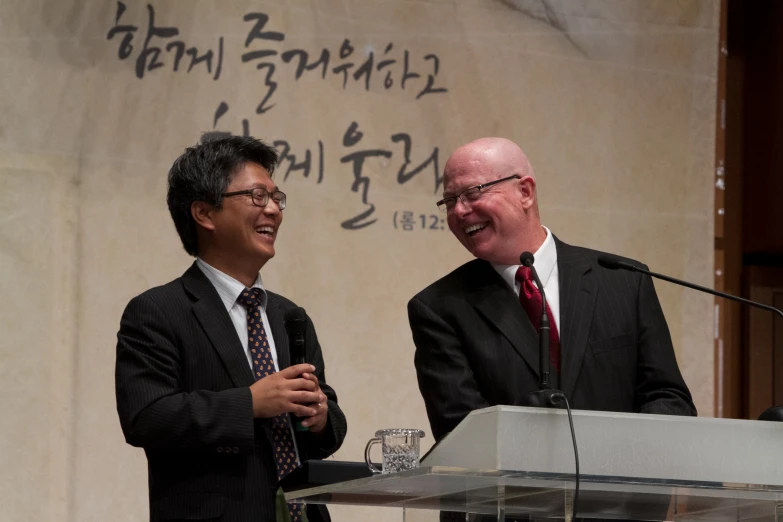 two men in business suits stand at a podium