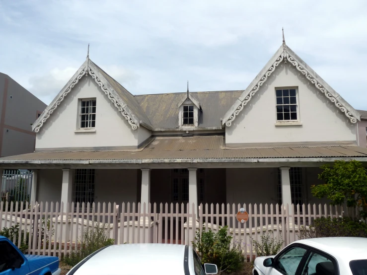 a small white house with a wooden fence and two cars parked