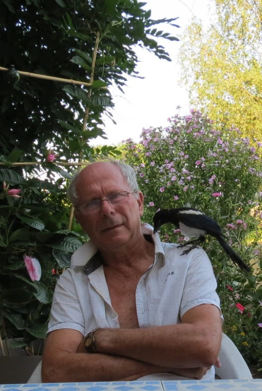 an elderly man sitting at a table with a bird on his shoulders