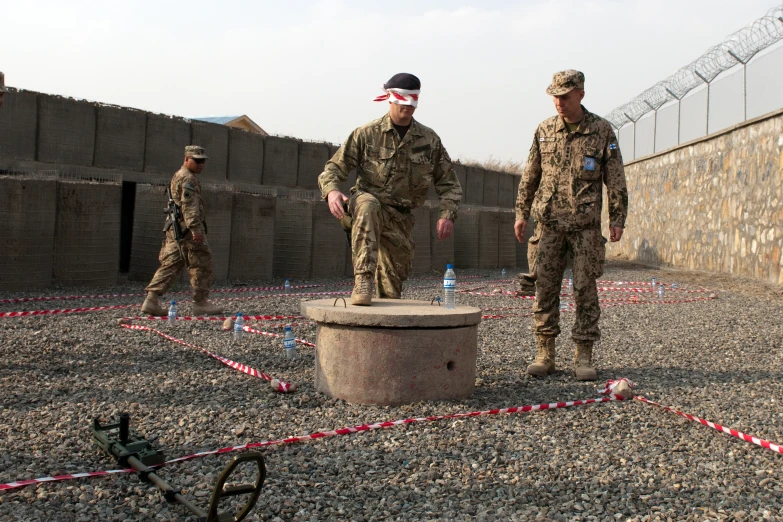 three uniformed soldiers in military fatigues walk around a cement structure