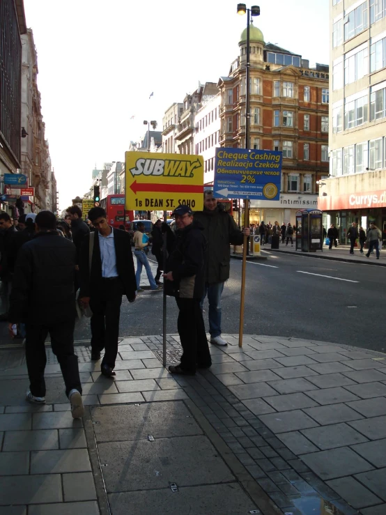 a group of people walking down a street next to a yellow and red sign