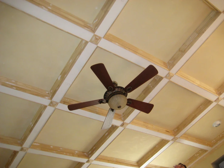 a ceiling fan with brown blades mounted in a room