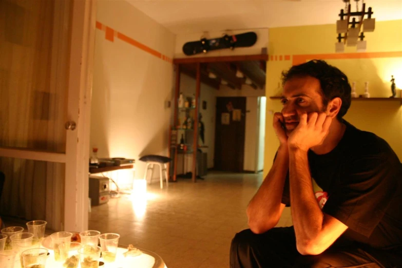 a man sitting on the floor with several glasses on his table talking on a cellphone