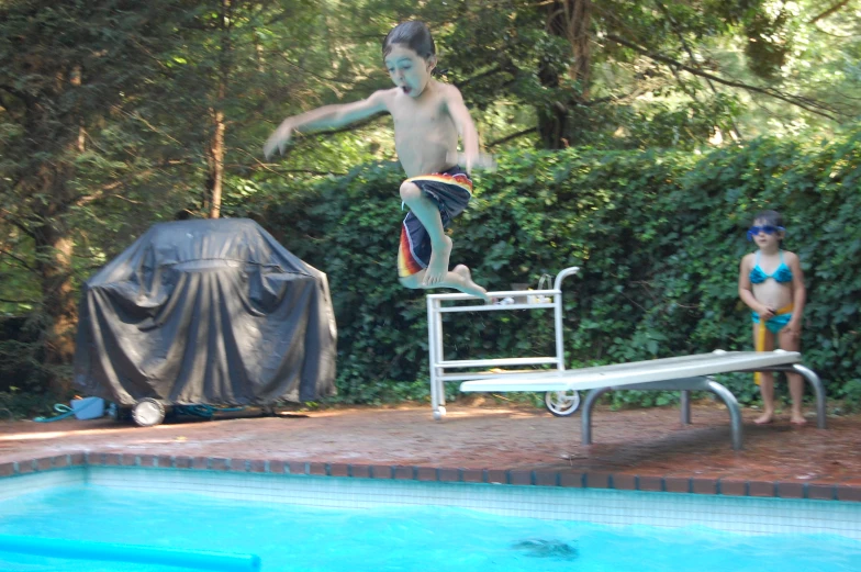 a young man is jumping into a pool next to another 