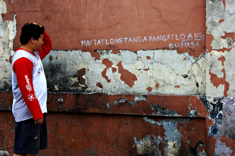 a young man standing next to a faded building wall