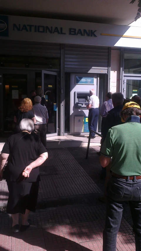 several people are walking along a sidewalk outside of an atm