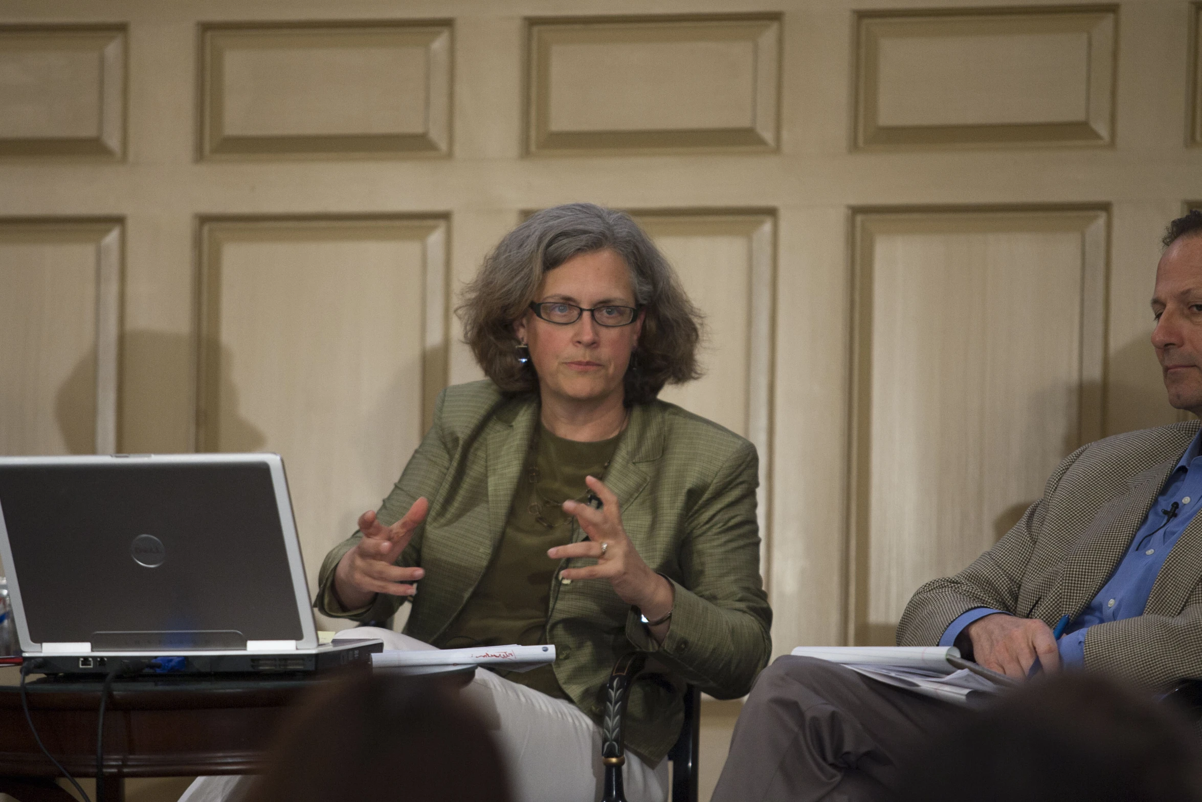 a woman talking in front of a laptop computer and another person standing next to her