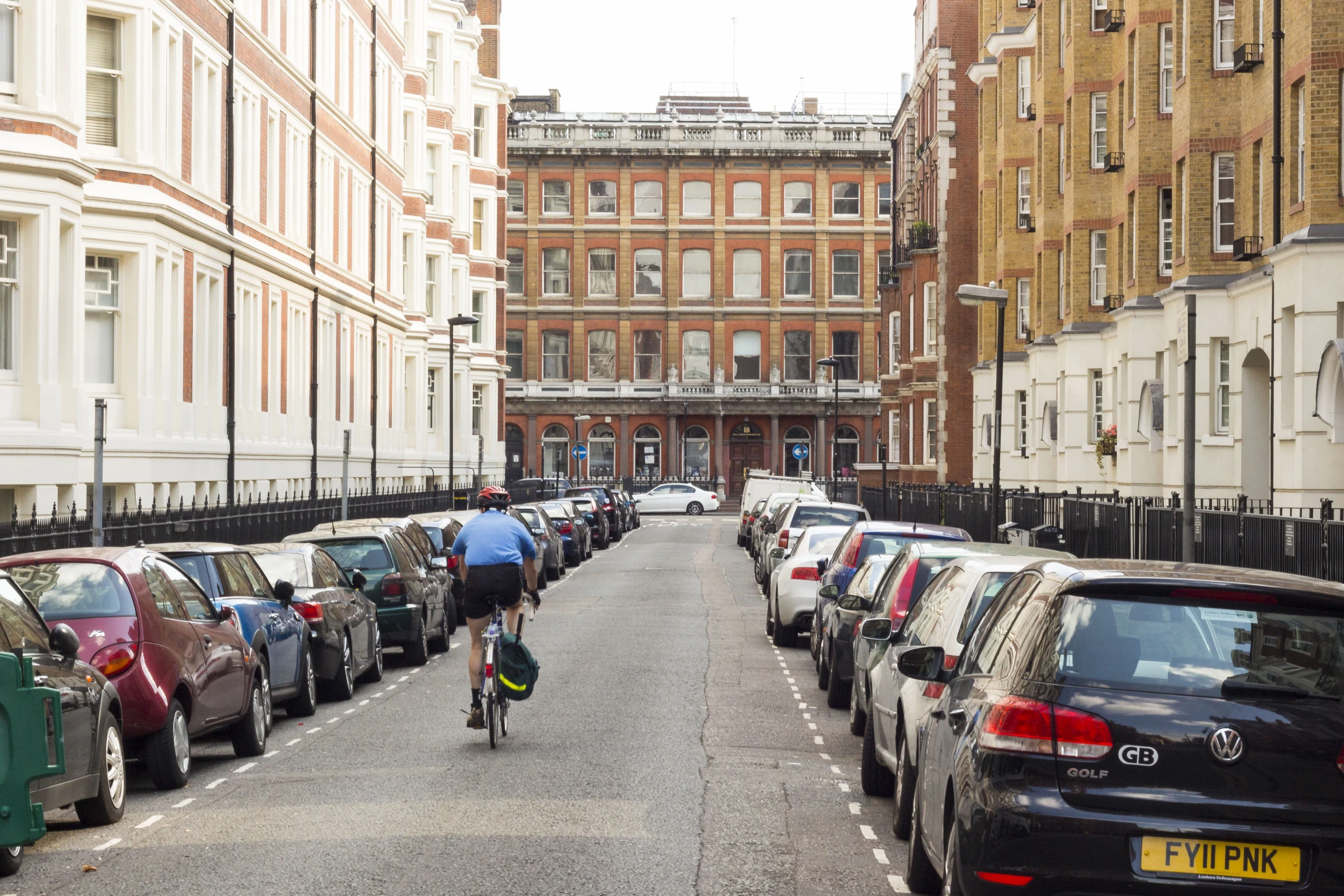 a cyclist rides on the street between several parked cars