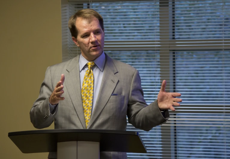 a man in a gray suit and yellow tie giving a talk