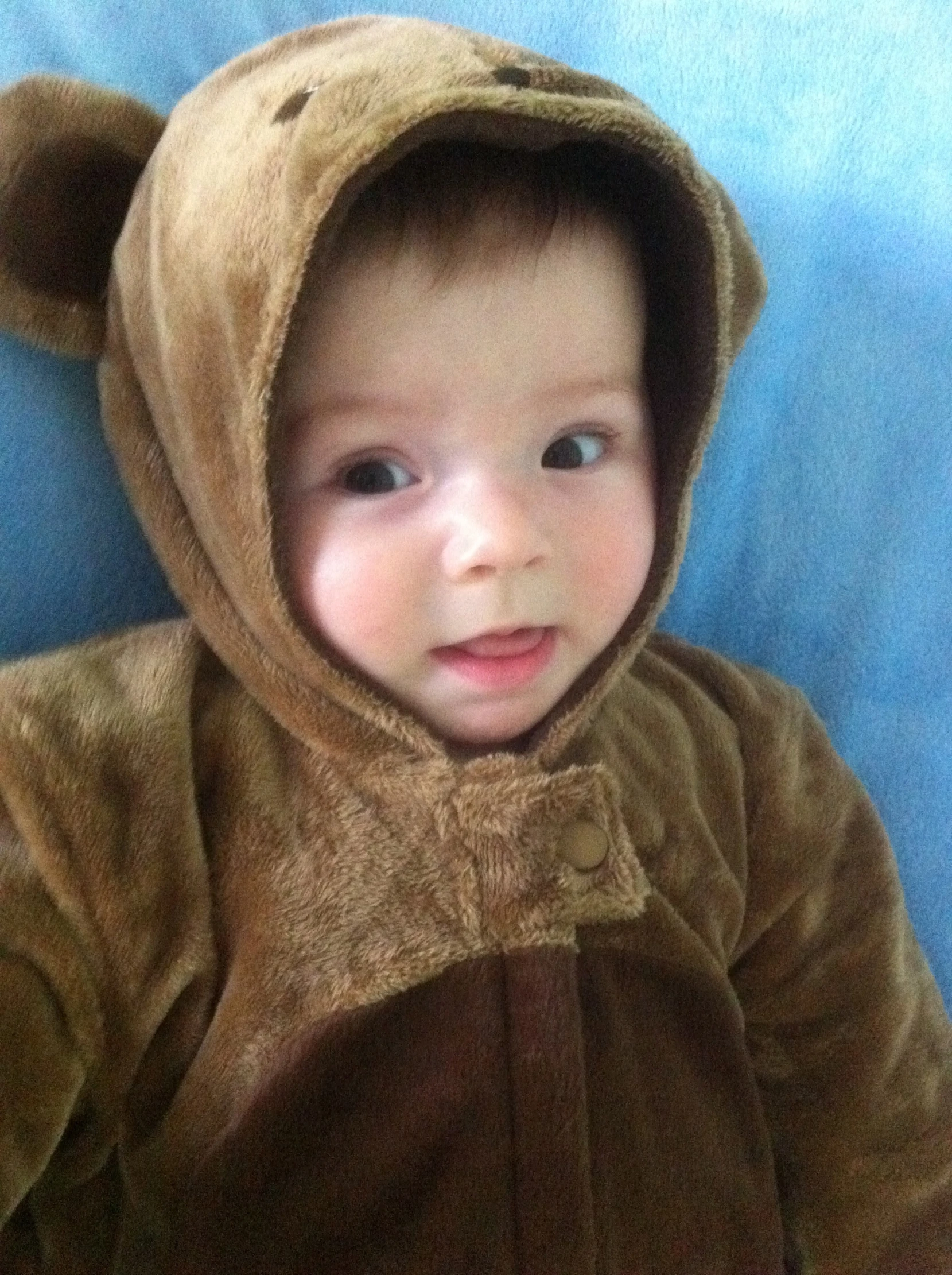 small child with hooded brown bear outfit sitting on bed