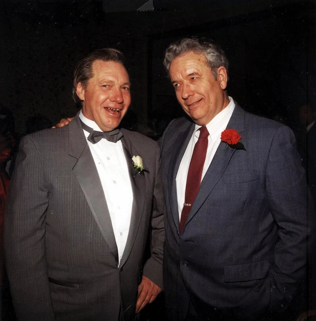 two men standing next to each other dressed in suits and ties