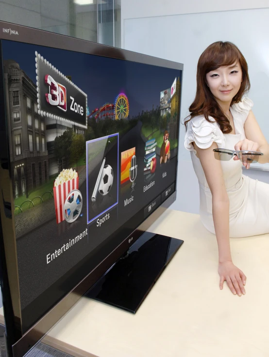 an asian woman sits on a desk in front of a flat screen tv