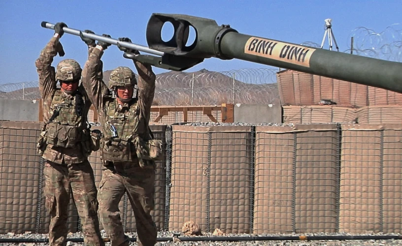 two soldiers holding a large black object while wearing camouflage