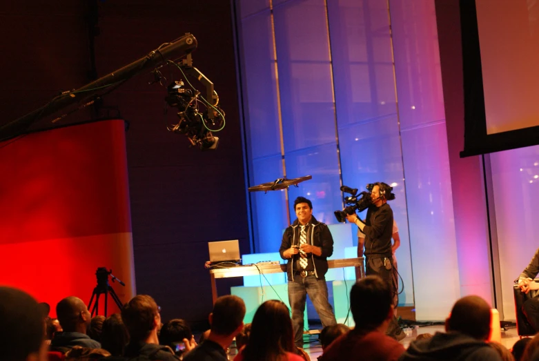 a couple of men stand on a stage as another person is recording them