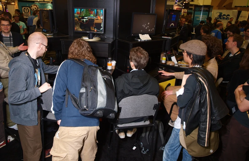 many people with backpacks standing near each other and in a room full of television monitors