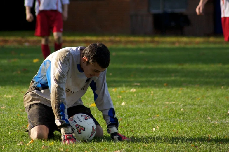 a boy kneeling down in the grass playing soccer