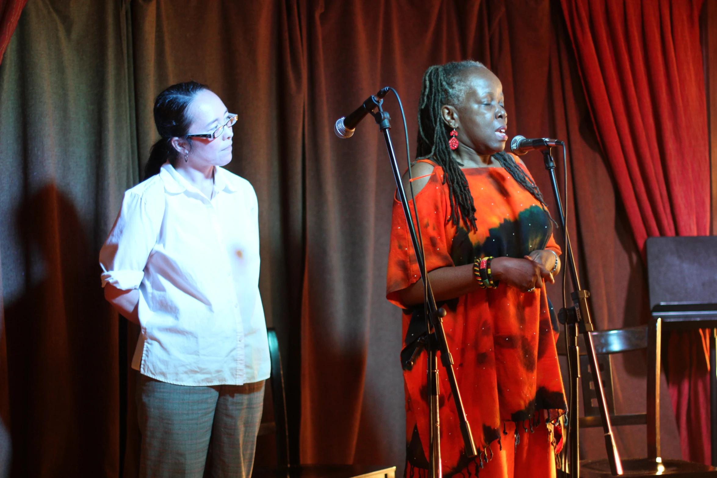 two women standing in front of red curtains and wearing glasses