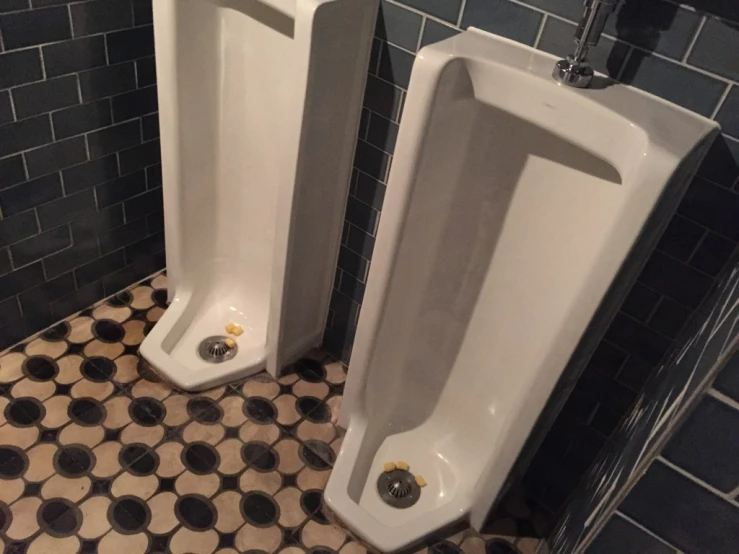 two urinals that are in a bathroom with tiled floors