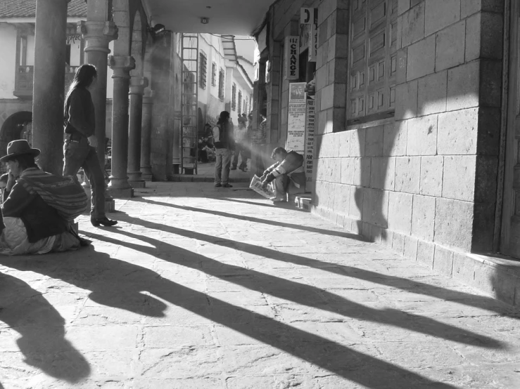 a person sits and reads near a woman with a hat on a city street