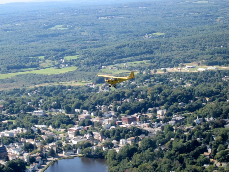 an aerial view of a small plane flying over trees and a town