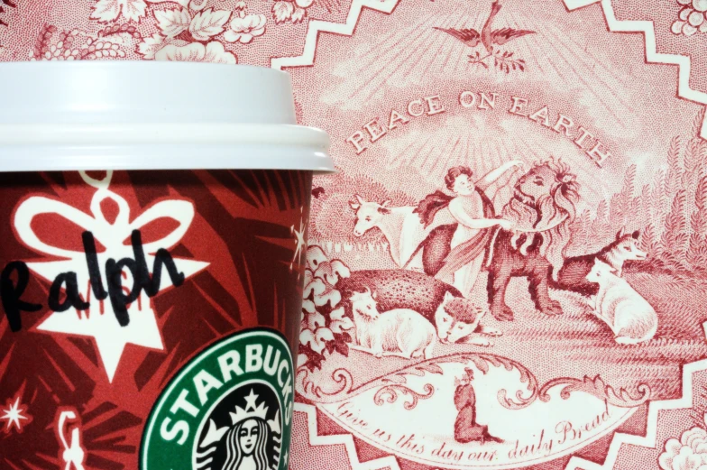 a starbucks cup sitting on a red and white tablecloth with a picture of a christmas tree