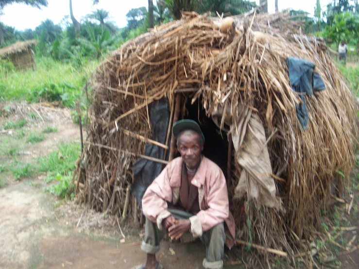 there is a man sitting in the doorway of a shelter made from straw