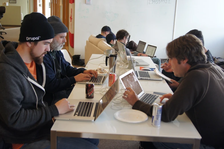 a group of people sitting around a table with laptops