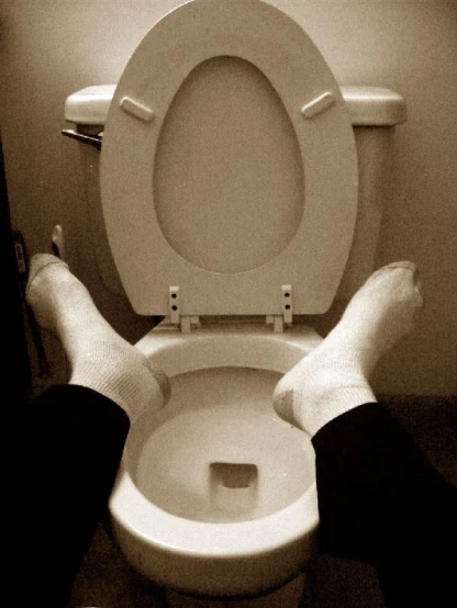the person sitting on the toilet has their legs up to the open seat