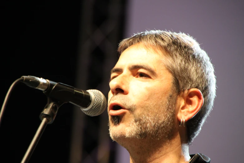 man with short grey hair sings into microphone