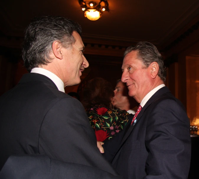 two men in suits talk to each other in an ornate room